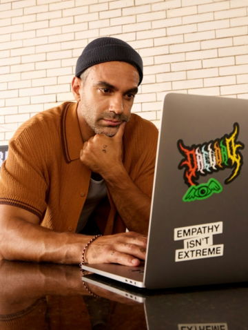 Man wearing a beanie and shirt works on a laptop.